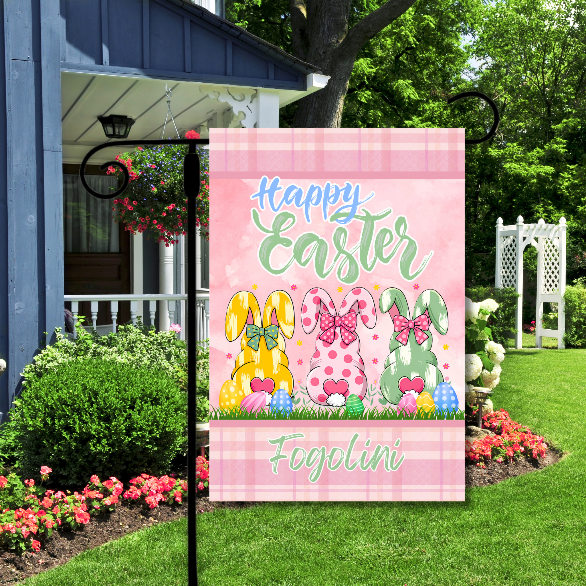 Happy Easter garden flag with bunnies and eggs on a pink checkered background, displayed outdoors.