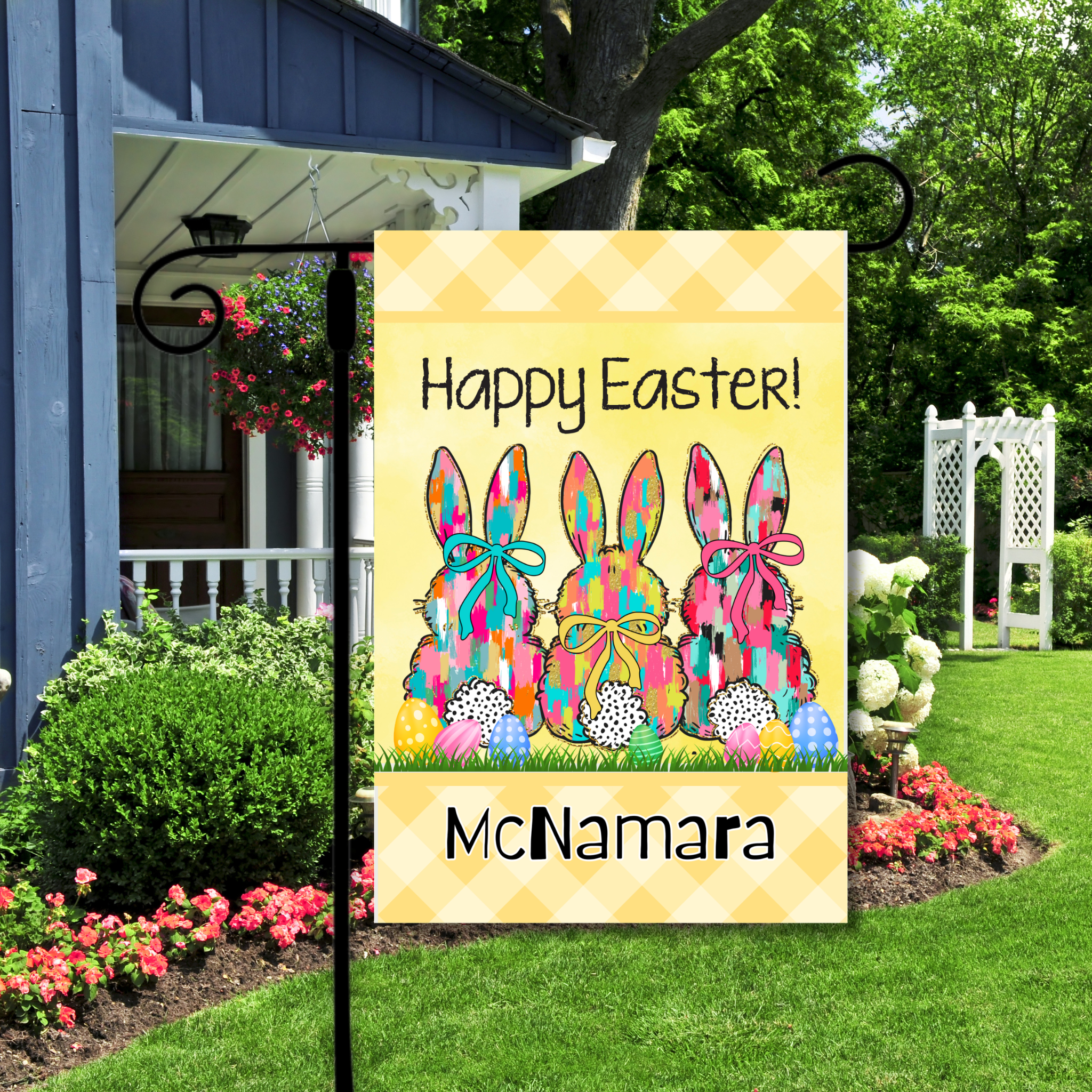 Decorative garden flag with colorful bunnies and 'Happy Easter!' text in a garden setting.