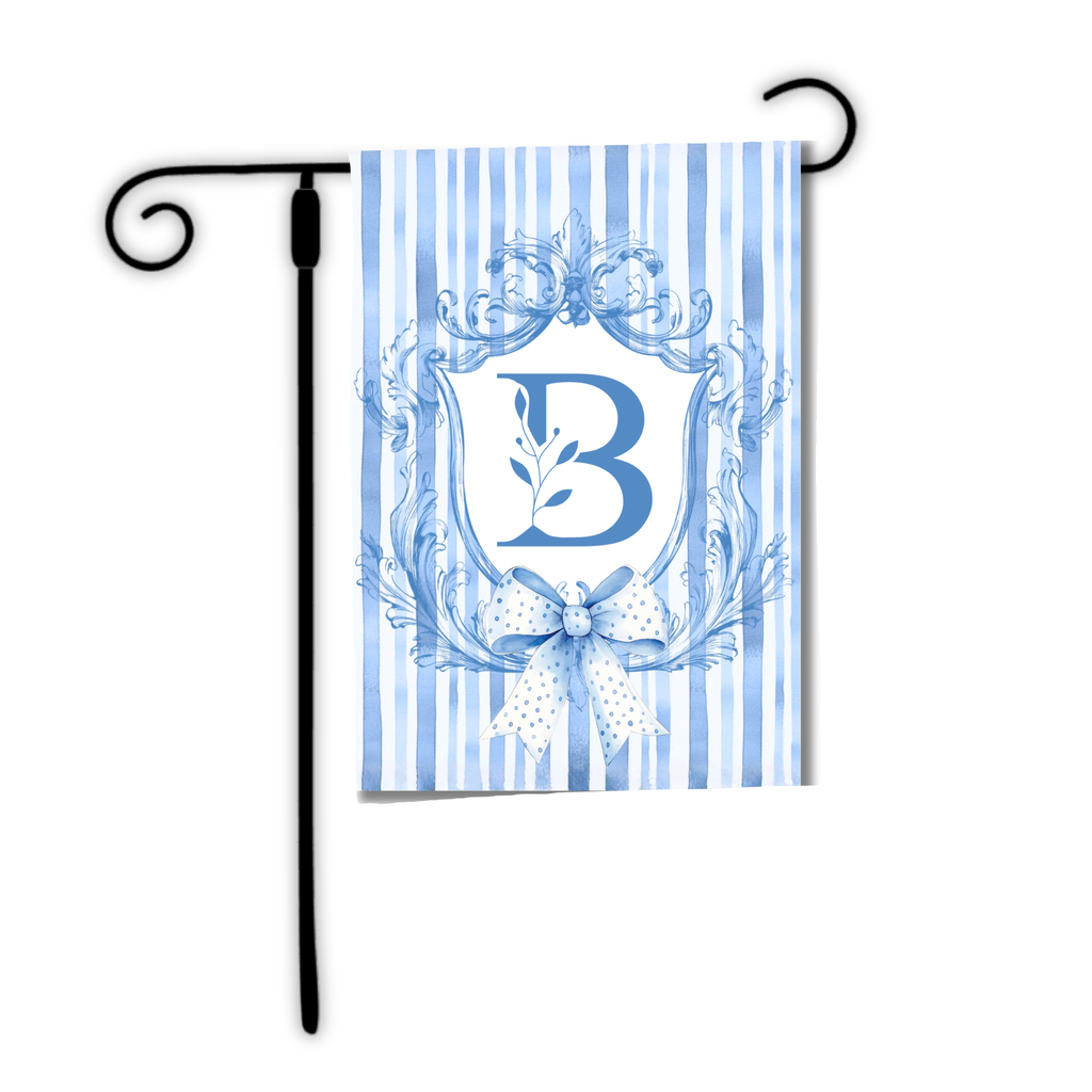 Decorative garden flag with blue letter 'B' and bow design on a striped background, attached to a black flagpole.