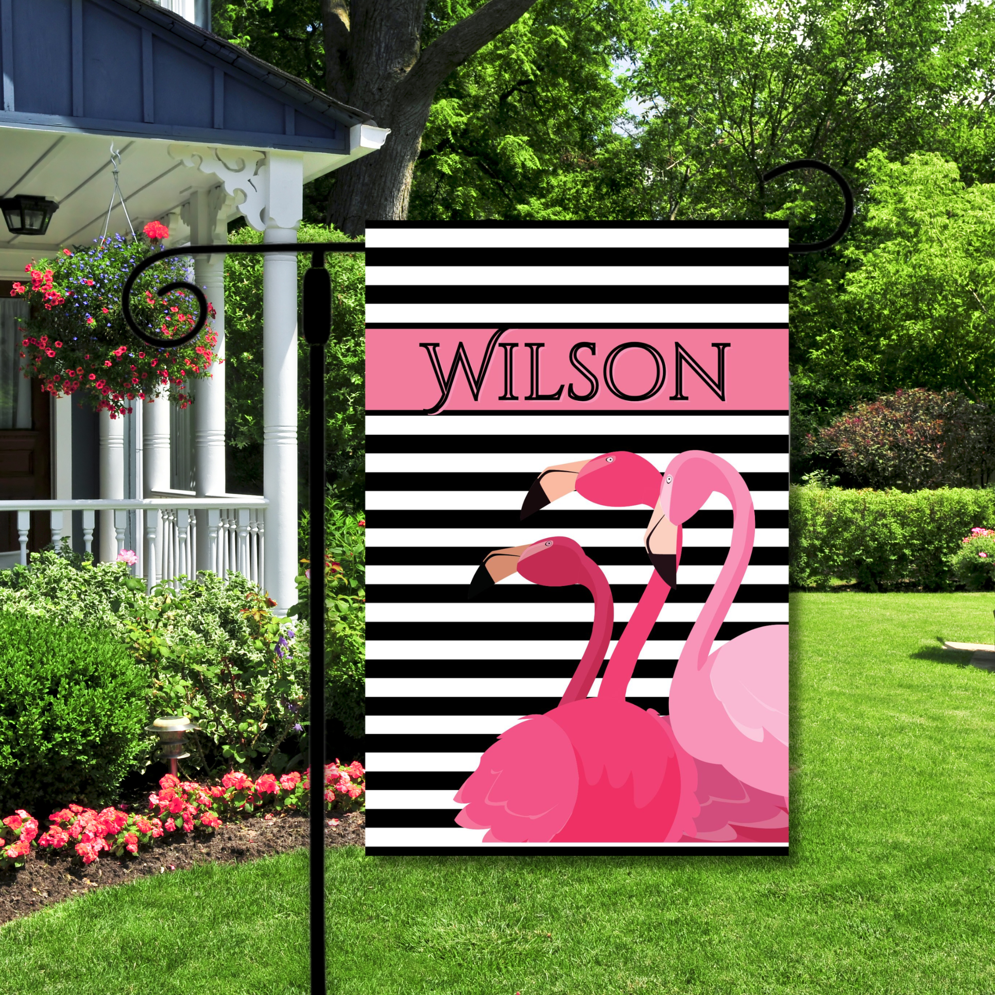 Garden flag with pink flamingos and black and white stripes, featuring the name 'Wilson', in a garden setting.