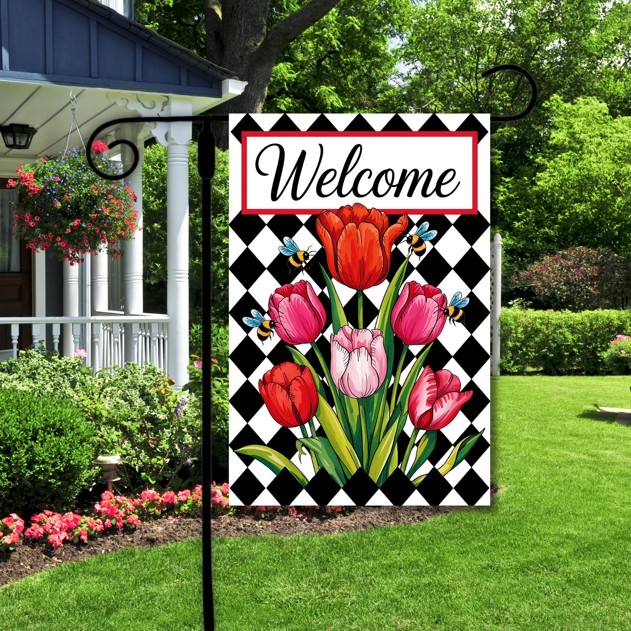 Decorative garden flag with tulips and 'Welcome' text in a checkered border, displayed outdoors.