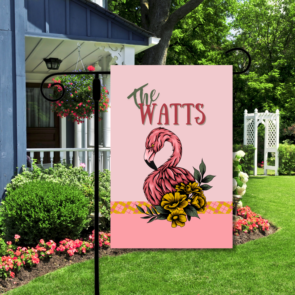 Decorative garden flag with flamingo design and 'The Watts' text in a garden setting.
