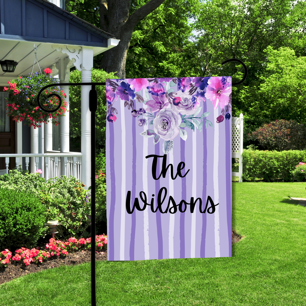 Decorative garden flag with floral design and 'The Wilsons' text in a garden setting.